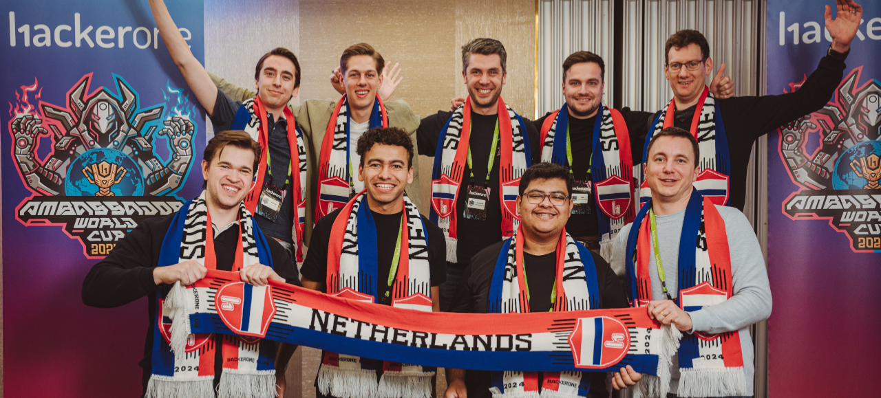 A group photo of the Dutch team celebrating at a HackerOne live-hacking event, holding a red, white and blue scarf. Co-founder of Skuridat, Mateus, bottom row, second from the left