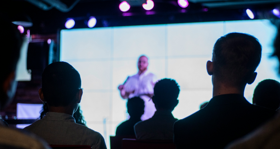 Silhouetted audience watching a speaker present on stage at a business conference