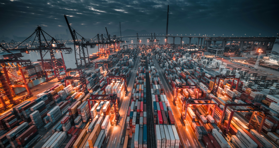 Illuminated shipping containers and gantry cranes at a busy port at night, representing global supply chains